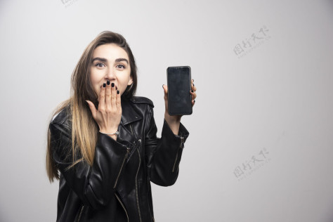 模特穿着皮夹克的女孩拿着灰色背景的智能手机头发女人衣服