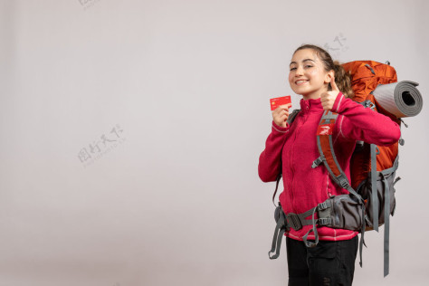 肖像微笑着的年轻旅行者 背着大背包 举着卡片制作大拇指招牌大人制造