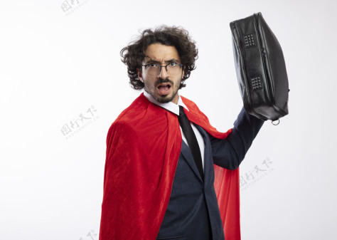 年轻人笨手笨脚的年轻超级英雄 戴着眼镜 穿着红色斗篷的西装 手里拿着一个孤立在白墙上的皮包眼镜穿着皮革