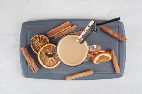 热美味的咖啡 肉桂棒和橘子片放在深色盘子里一餐咖啡因美味
