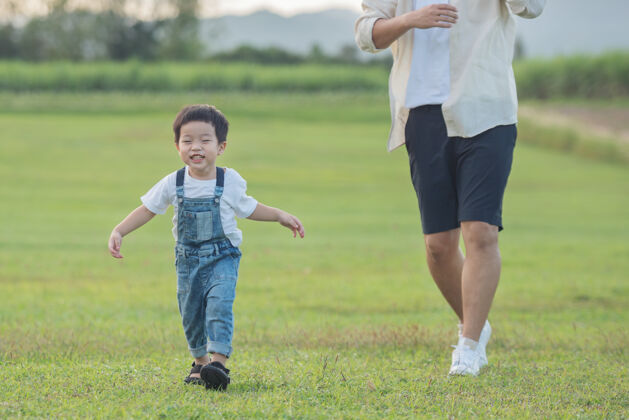 阳光夕阳时分 父子俩在公园里玩耍人们在球场上玩得很开心友好家庭和暑假的概念父子俩的腿穿过公园的草坪人孩子周末