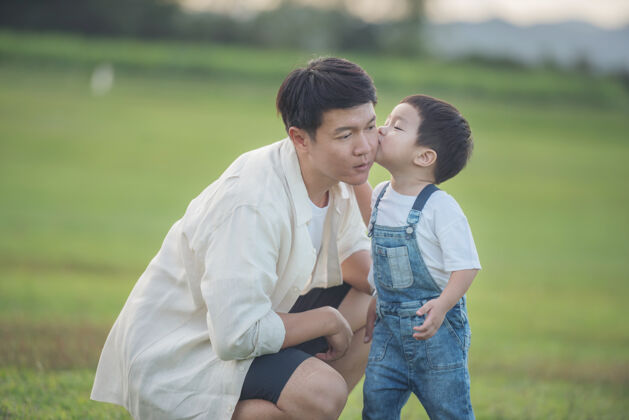 自由夕阳时分 父子俩在公园里玩耍人们在球场上玩得很开心友好家庭和暑假的概念父子俩的腿穿过公园的草坪玩耍一天亚洲