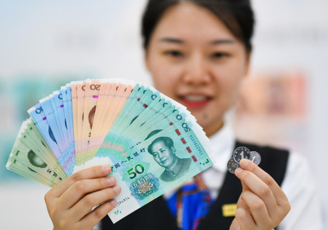 Seorang wanita menunjukkan wang kertas dan syiling edisi 2019 siri kelima Renminbi （foto/Xinhua)