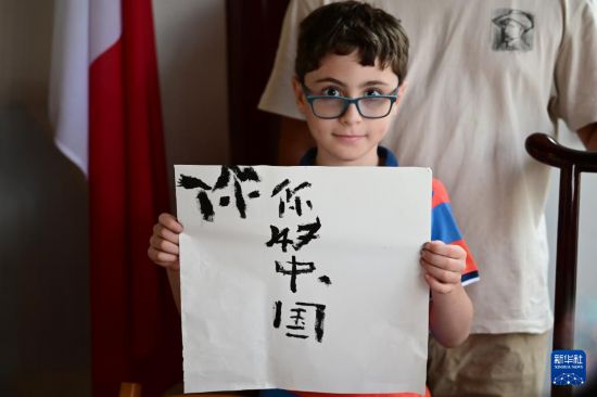7月4日，在马耳他桑塔露琪亚市的中国古典园林“静园”，一名男孩展示他的书法作品。新华社发（乔纳森·博格 摄）