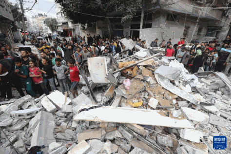 5月14日，在加沙地带中部努赛赖特难民营，人们查看以军轰炸后的建筑废墟。新华社发（巴勒斯坦通讯社供图）