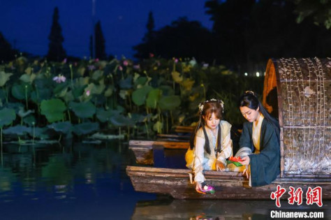 江蘇省南京市高淳区にある固城湖水慢城のハス池で、ハスの灯篭に火をつける伝統衣装姿の若者（6月29日撮影・泱波）。